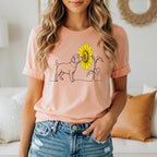 Peach t-shirt with minimalist line art of a dog smelling a sunflower.