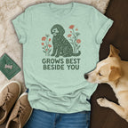 Sage green t-shirt featuring a curly dog illustration and the text GROWS BEST BESIDE YOU.