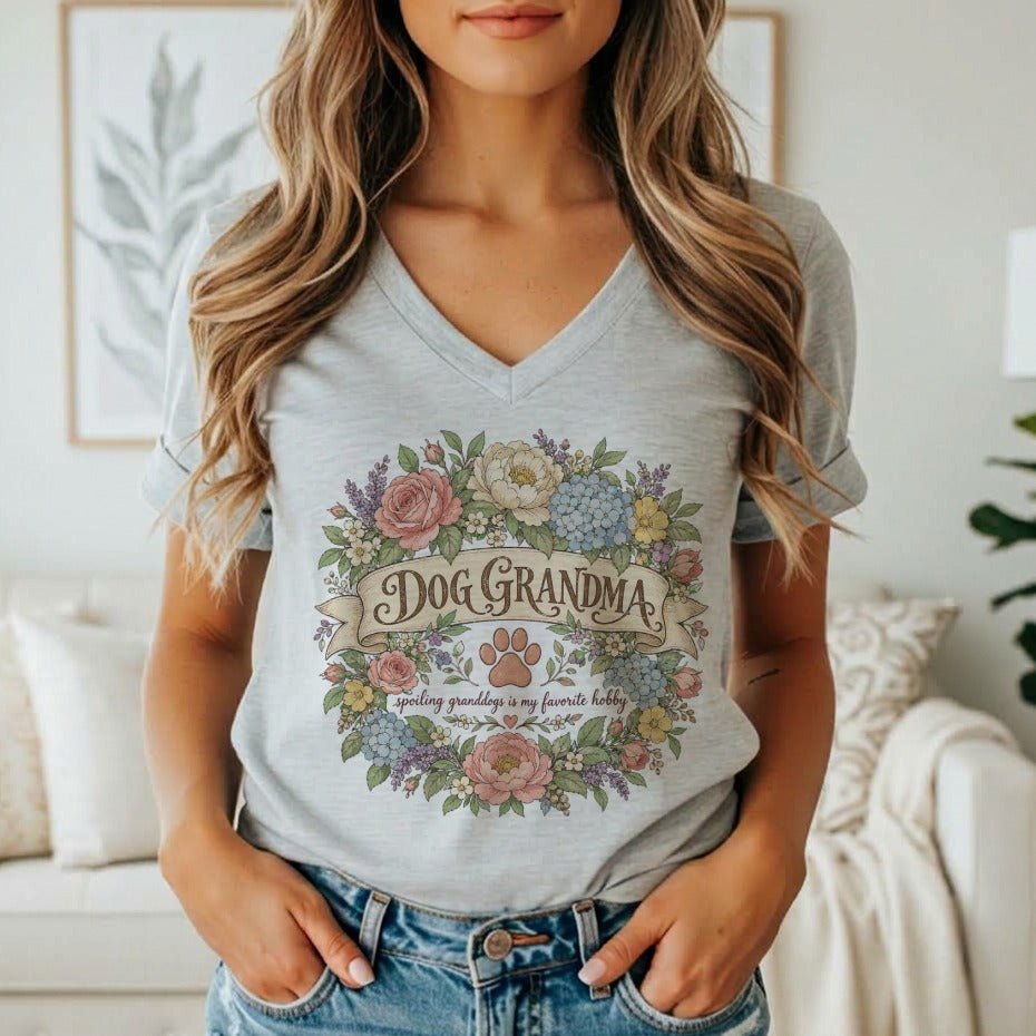 A woman wearing a gray V-neck t-shirt featuring a floral wreath, paw print, and the text Dog Grandma.