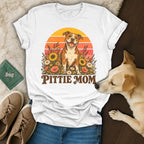 A white t-shirt featuring a retro Pitbull graphic that reads "Pittie Mom" above sunflowers and a sunset.