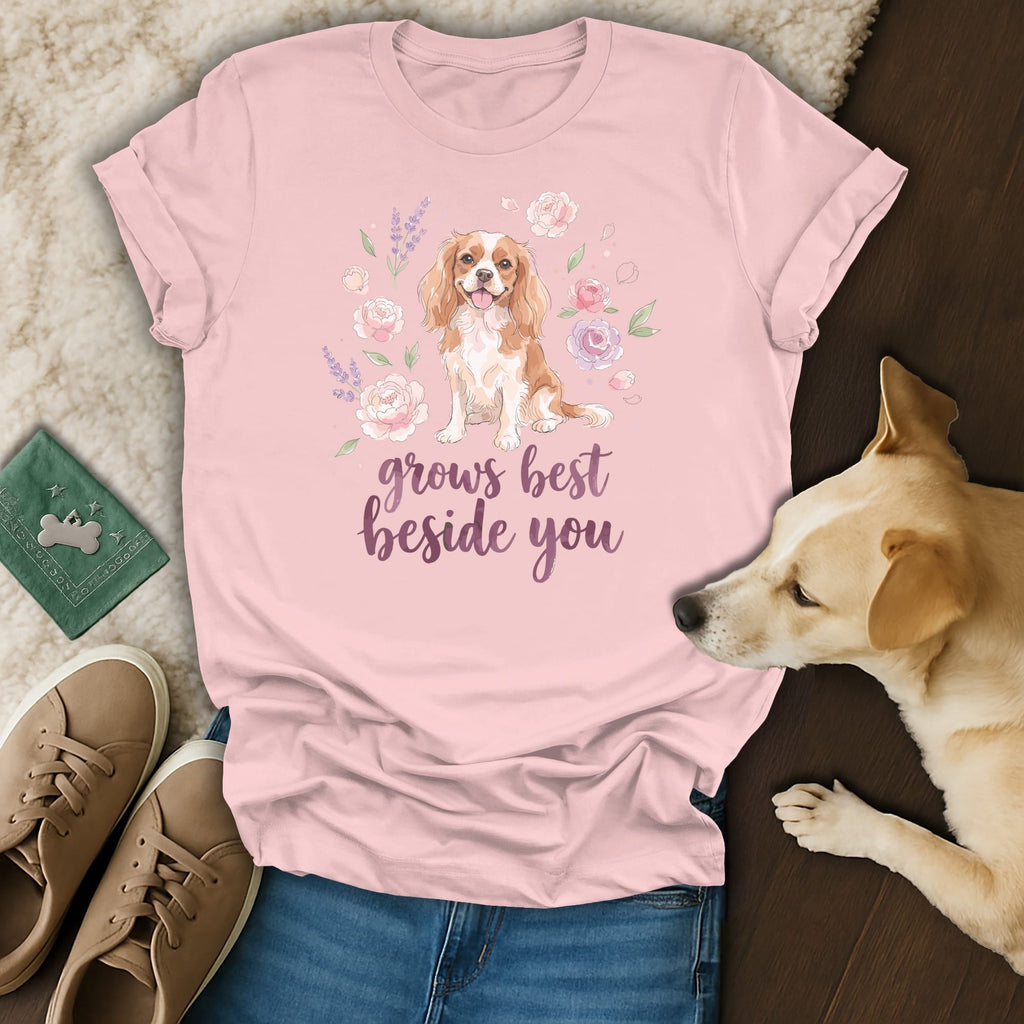 A pink t-shirt with a Cavalier King Charles Spaniel graphic and the text grows best beside you.