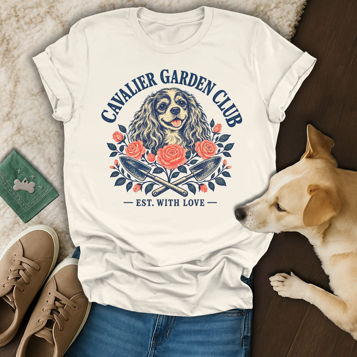 A cream t-shirt with a Cavalier Garden Club graphic featuring a dog, roses, and crossed garden trowels.