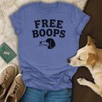 Blue t-shirt with "FREE BOOPS" and dog head graphic, flat lay with dog and sneakers.