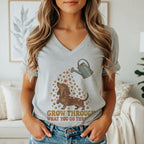 A woman wearing a heather gray V-neck t-shirt printed with a dachshund watering can design and text.