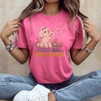 A woman wearing a pink t-shirt with a graphic of a puppy blowing dandelion seeds and the text Wish Big, Wag Bigger.