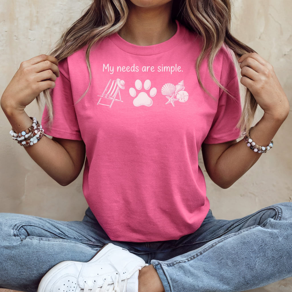 Pink t-shirt with text "My needs are simple" and graphics of beach chair, paw, and shells.