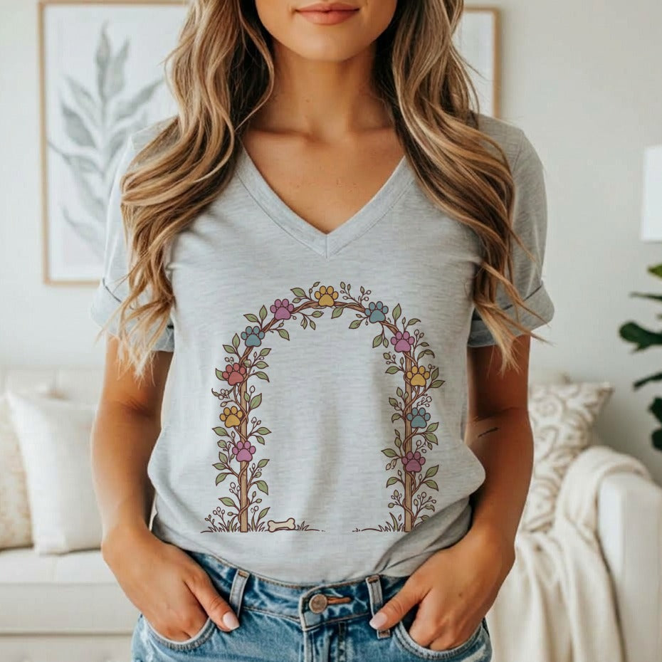 A woman wearing a gray V-neck t-shirt featuring a floral arch graphic with colorful paw prints.