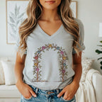 A woman wearing a gray V-neck t-shirt featuring a floral arch graphic with colorful paw prints.