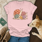 Pink t-shirt with a cartoon graphic of colorful snails featuring paw prints on their shells.