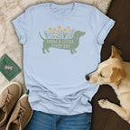 Light blue t-shirt featuring a green dachshund graphic with yellow flowers and the text Grow a little every day.