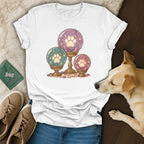 A white t-shirt featuring a magical crystal ball paw print graphic rests on a wooden floor near a dog and shoes.