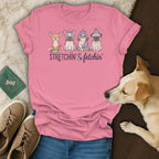 Pink t-shirt with four dogs wearing spa accessories and text "Stretchin' & fetchin'".