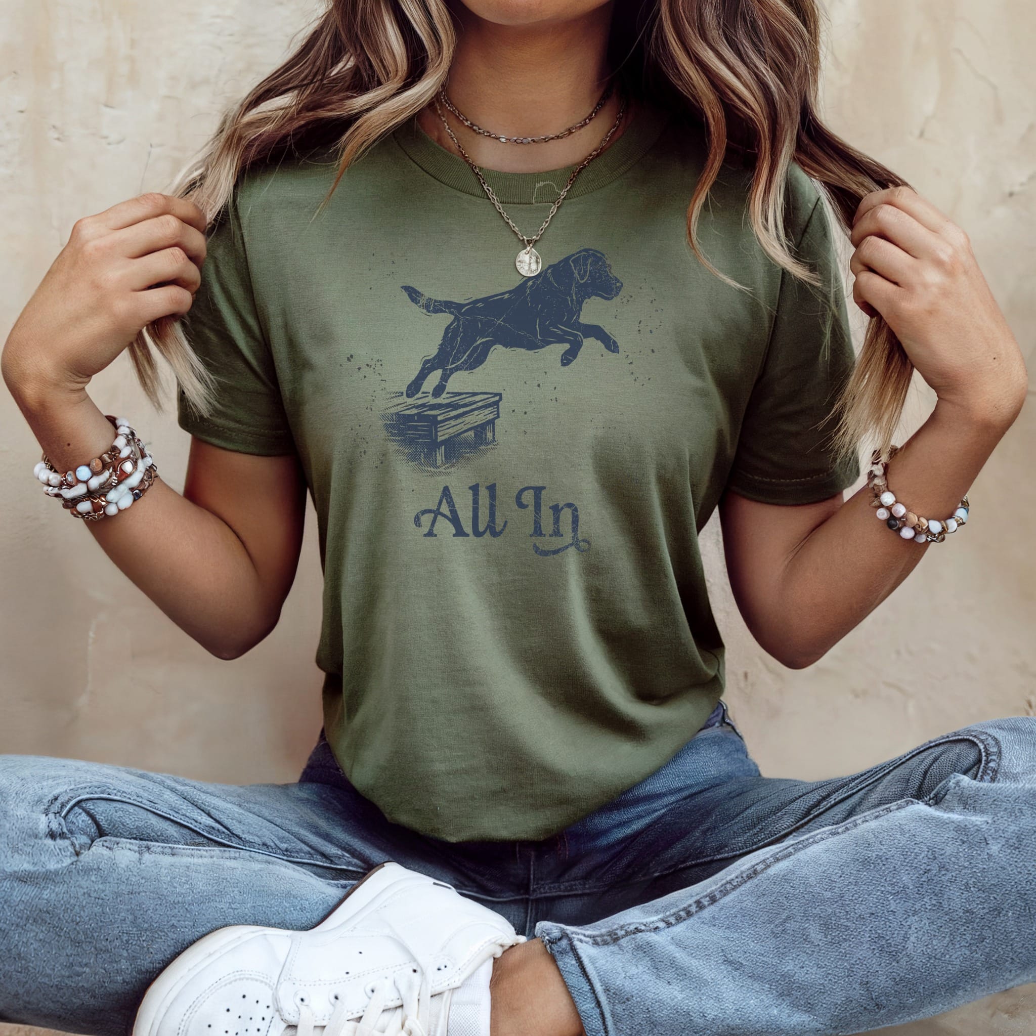 Dog jumping onto platform with "All In" text on olive green t-shirt.