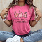 A person wearing a pink t-shirt with illustrations of three dogs, flowers, and the text "FUR BABIES FLOWER BEDS".
