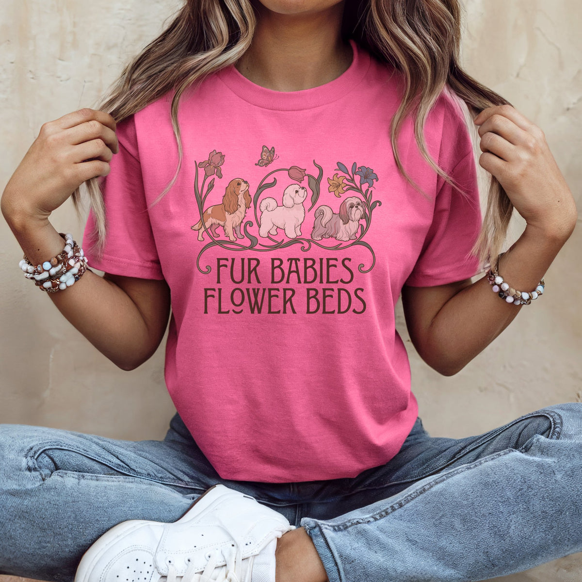 A person wearing a pink t-shirt with illustrations of three dogs, flowers, and the text "FUR BABIES FLOWER BEDS".
