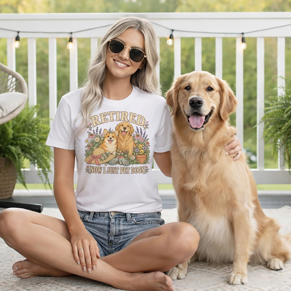 A blonde woman wearing sunglasses and a white graphic t-shirt sits smiling with a golden retriever.