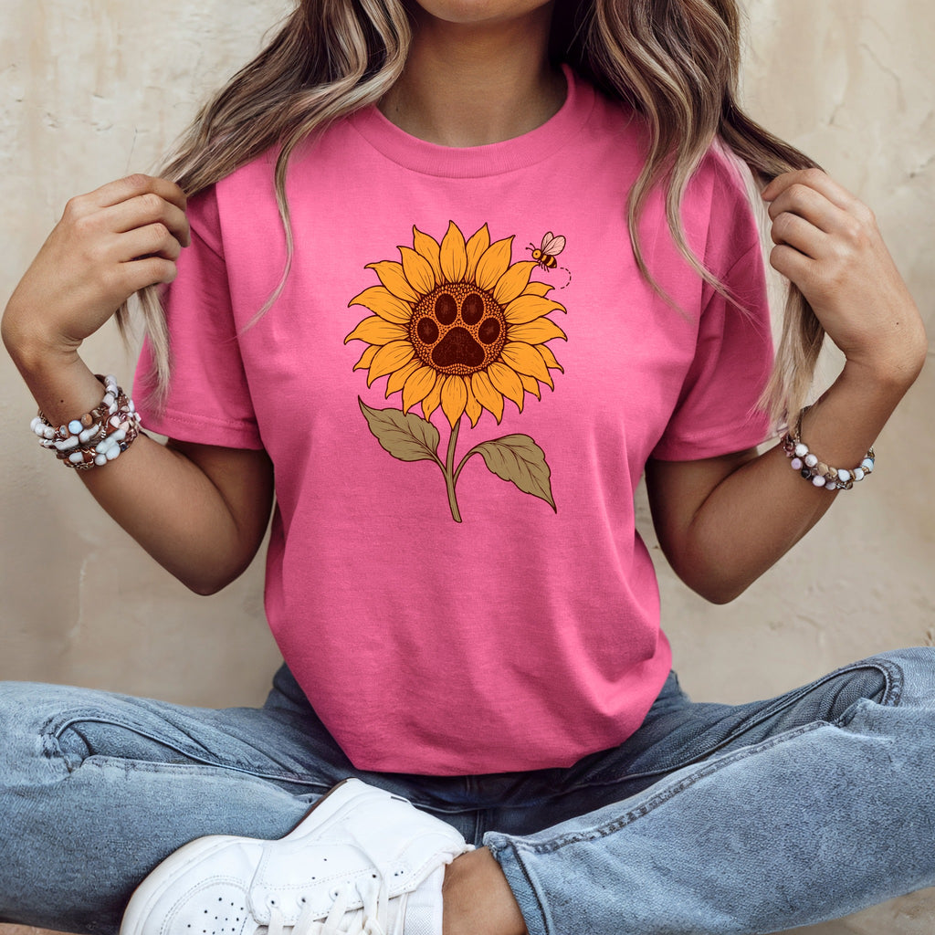 A person wearing a bright pink t-shirt with a sunflower graphic featuring a paw print center.