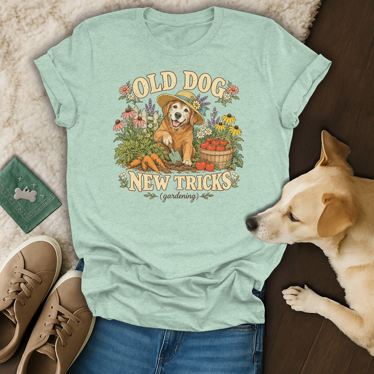 A light green t-shirt with a vintage-style graphic of a golden retriever gardening, surrounded by shoes, jeans, and a real dog.
