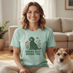 A smiling woman wearing a mint-green t-shirt with a dog illustration and the text GROWS BEST BESIDE YOU sits next to a Jack Russell Terrier.