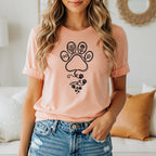 Peach t-shirt with a black line art design of paw prints, flowers, and infinity symbol.
