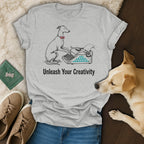 T-shirt with a dog wearing a bowtie typing on a typewriter, text "Unleash Your Creativity".