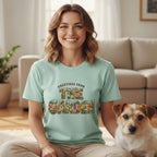 A smiling woman wearing a mint-green t-shirt with floral graphics and a small dog sitting beside her.