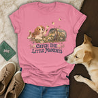 A pink t-shirt featuring a graphic of a puppy, flowers, bees, and the text Catch the Little Moments.