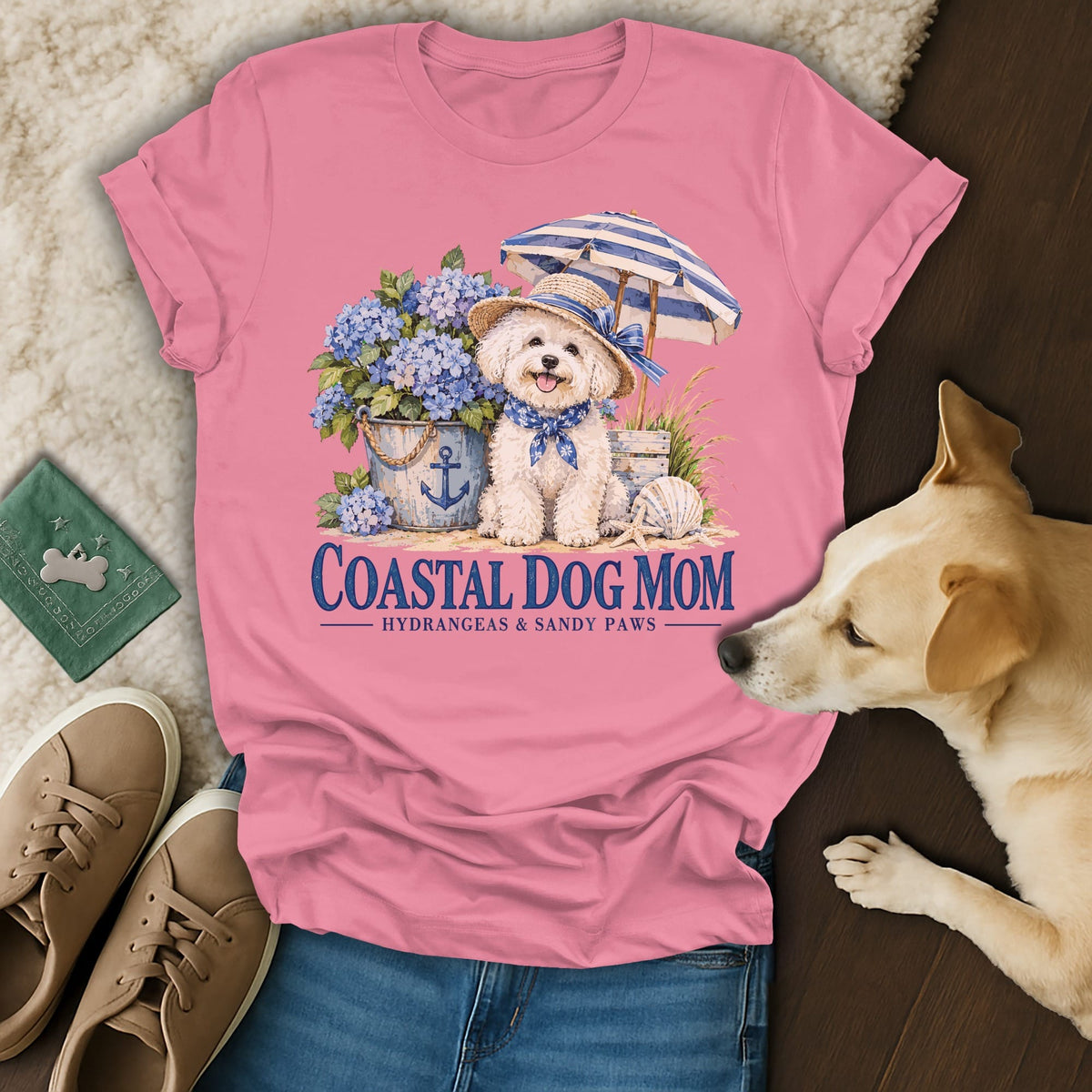 Pink t-shirt with a graphic of a dog wearing a sun hat beside hydrangeas, featuring the text Coastal Dog Mom.