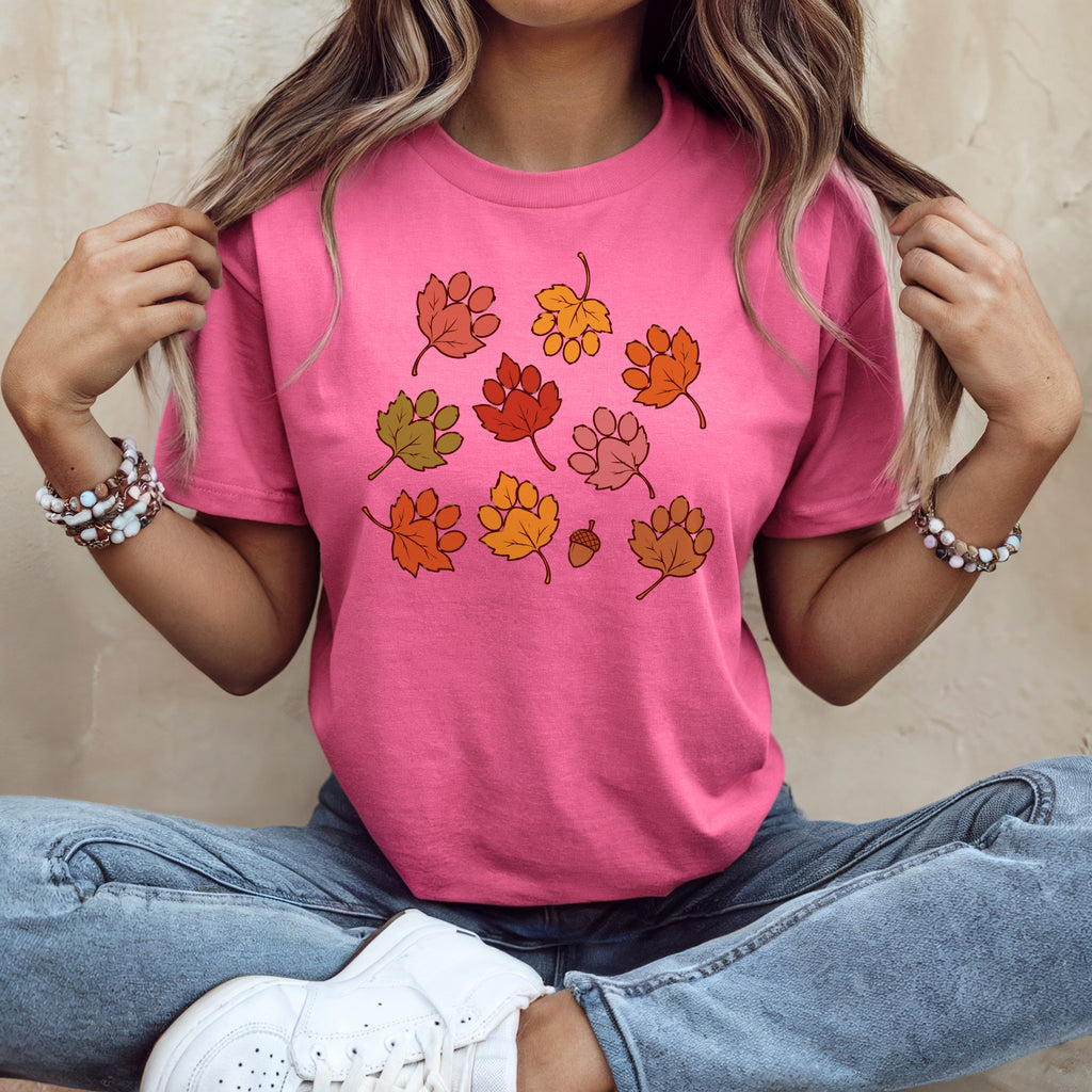 A woman wearing a pink t-shirt with autumn paw print leaf graphics and blue jeans.