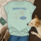 Light green t-shirt with cartoon dog playing ball, "HAVING A BALL is kind of my thing."