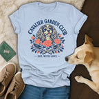 Light blue t-shirt featuring a Cavalier King Charles Spaniel graphic with flowers and gardening tools.