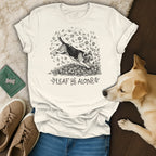 T-shirt graphic of a beagle jumping through fall leaves with the text "LEAF ME ALONE".