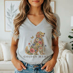 A woman wearing a grey V-neck t-shirt printed with a golden retriever graphic made of colorful flowers and the text "GOLDEN MAMA".