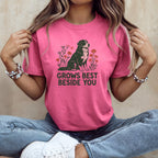 A person wearing a pink t-shirt with a graphic of a Bernese Mountain Dog and the text GROWS BEST BESIDE YOU.