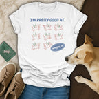 White t-shirt with "I'M PRETTY GOOD AT winging it" text and cartoon dogs with wings.