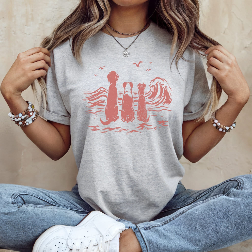 Three dogs and two cats sit facing a stylized ocean wave on a light gray t-shirt.
