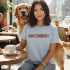 A woman with dark hair wearing a light blue t-shirt sits at a cafe table with a golden retriever beside her.