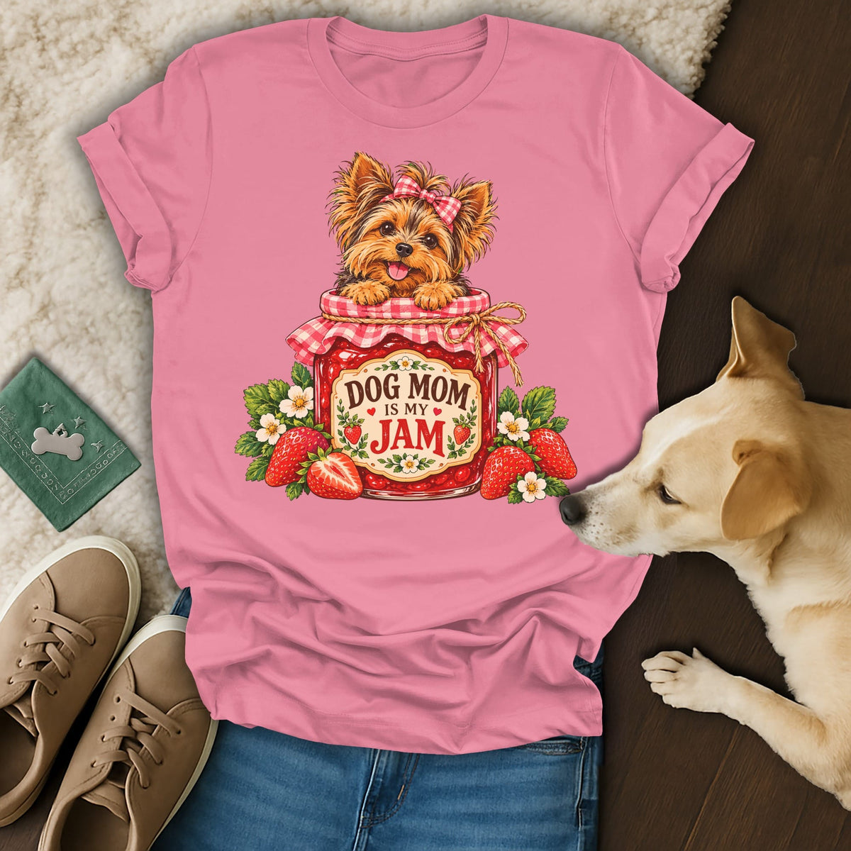 A pink t-shirt featuring a Yorkshire terrier inside a strawberry jam jar with text reading DOG MOM IS MY JAM, laid out with blue jeans, sneakers, and a real dog.