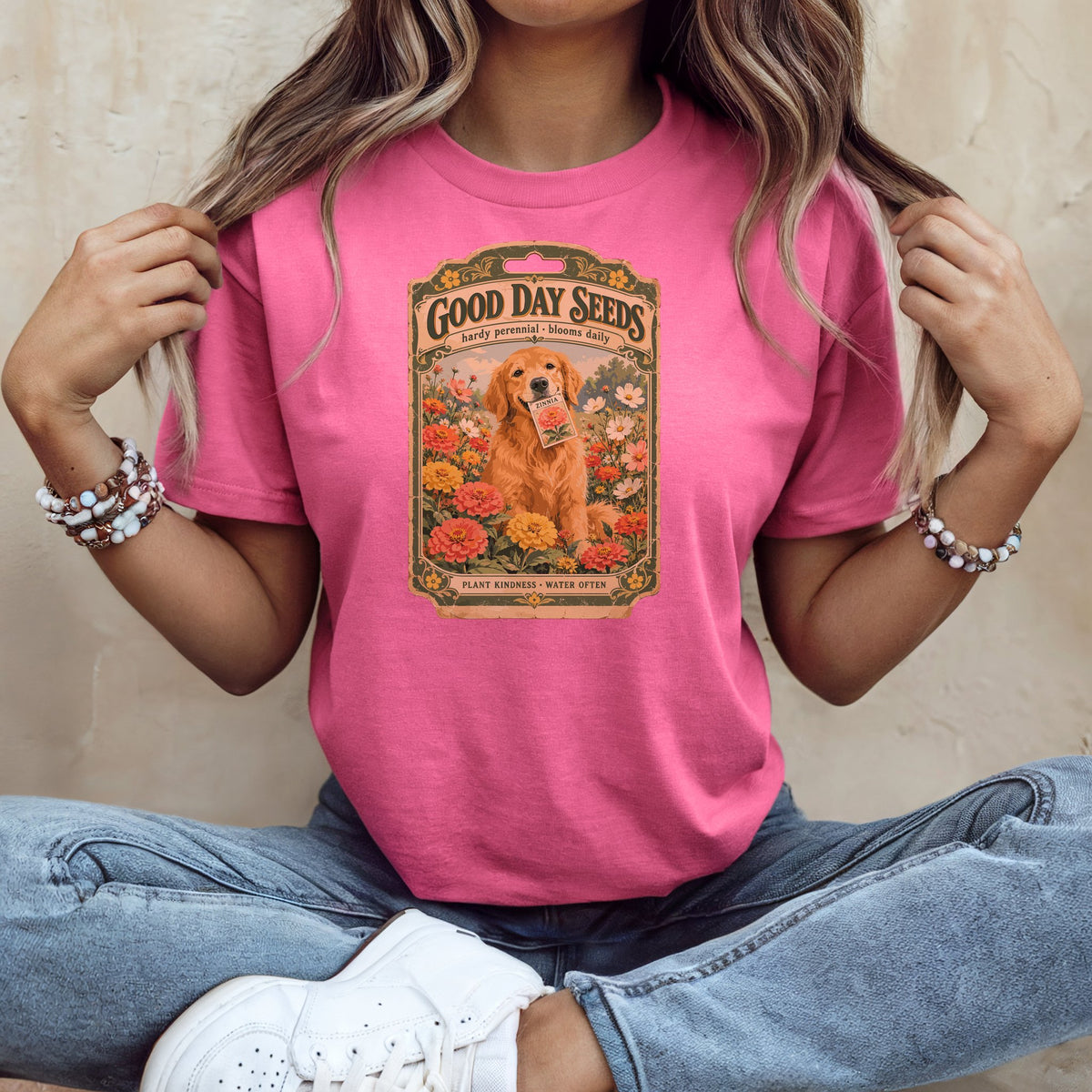 A woman wearing a pink t-shirt printed with a vintage seed packet graphic featuring a golden retriever.