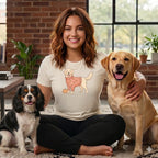 Woman wearing a cream t-shirt with a dog graphic and sitting with two dogs.