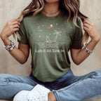 Olive green t-shirt with a cartoon dog on an island under a crescent moon.
