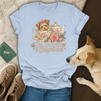 Light blue t-shirt featuring a vintage illustration of a puppy in a teacup with floral elements and text.