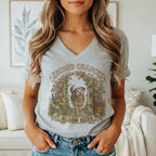 A woman wearing a gray V-neck t-shirt featuring a graphic of a dog, flowers, and the text Second Chances Bloom Here.
