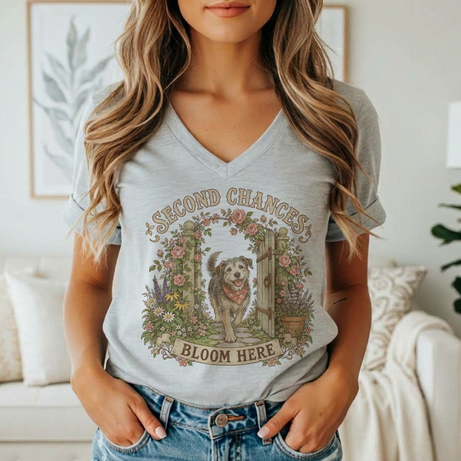 A woman wearing a gray V-neck t-shirt featuring a graphic of a dog, flowers, and the text Second Chances Bloom Here.