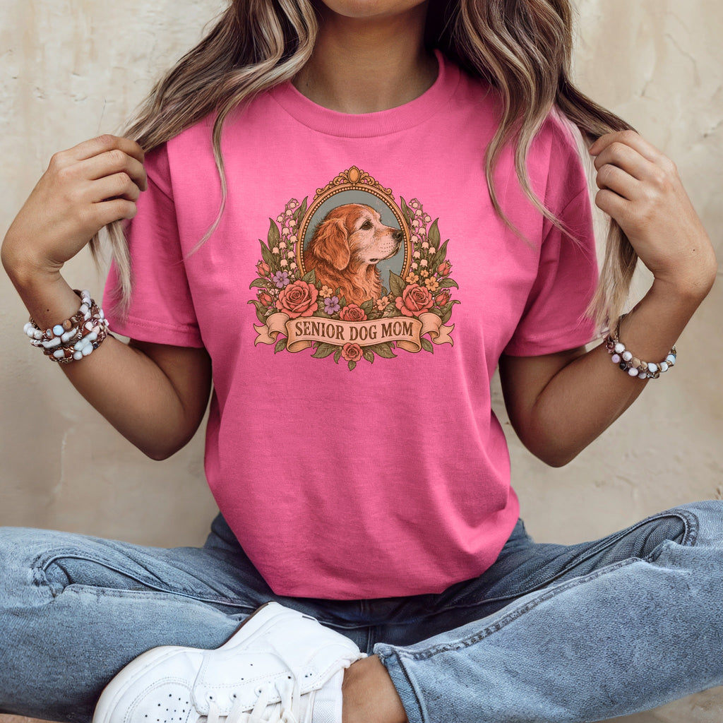 A person wearing a pink t-shirt with a vintage graphic of a dog, flowers, and the text SENIOR DOG MOM.