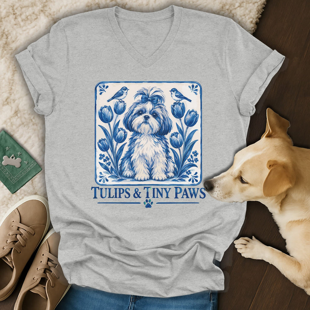 Gray V-neck t-shirt featuring a blue and white Delft-style illustration of a puppy, tulips, birds, and text reading Tulips & Tiny Paws.