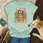 A light green t-shirt with a graphic of a dog in a flower pot and the text I ADOPTED AN OLD SOUL.