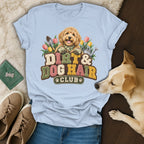 A light blue t-shirt with a graphic of a golden doodle, garden tools, and the text Dirt and Dog Hair Club.