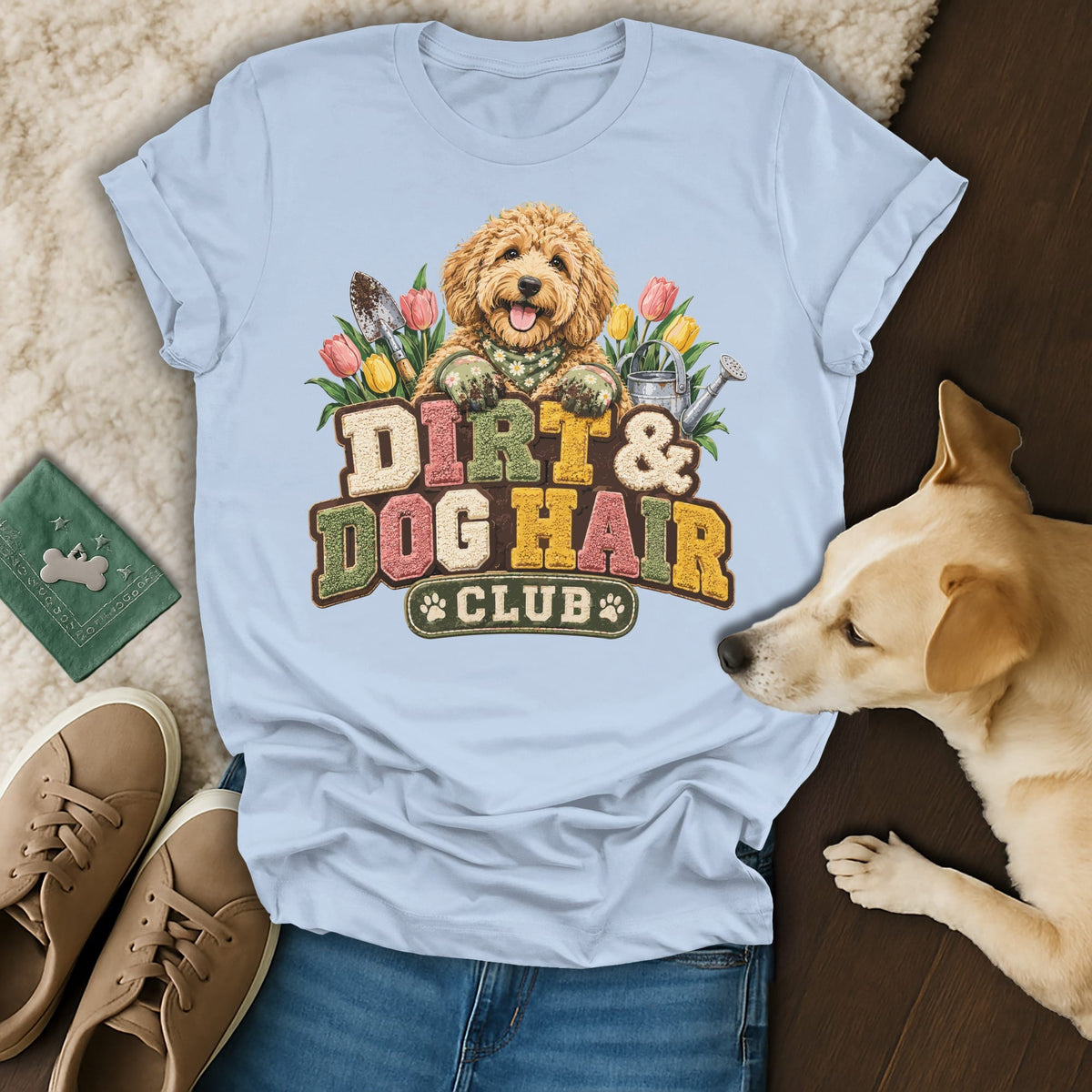 A light blue t-shirt with a graphic of a golden doodle, garden tools, and the text Dirt and Dog Hair Club.