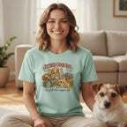 A smiling woman wearing a light blue t-shirt with a vintage dog graphic sits beside a small terrier in a living room.
